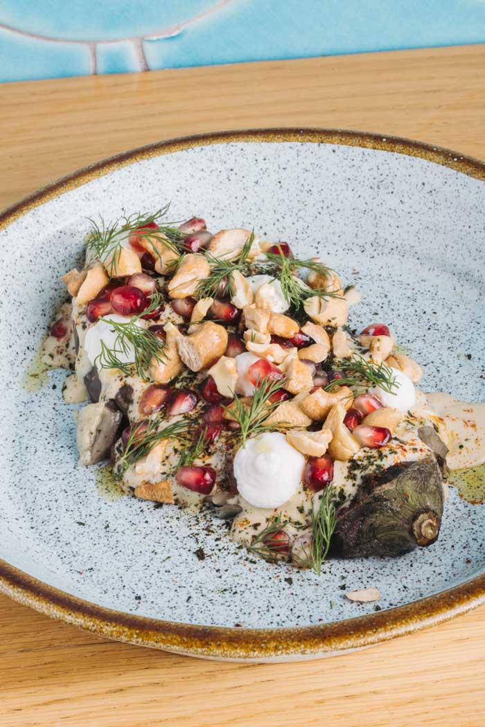 Berenjena a la brasa con aliño de sésamo de naranja, ricota, granada y hierbas frescas servida en Kulto Madrid